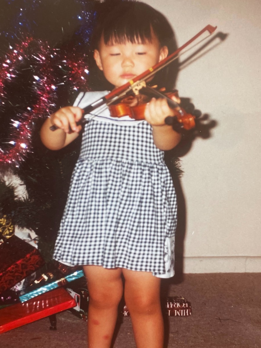 Emily Sun as a small child, playing her violin in front of a Christmas tree.