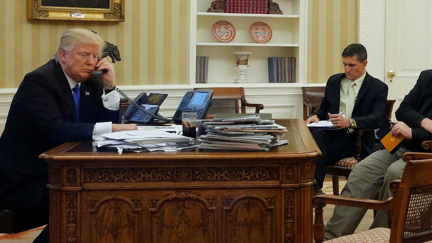 US President Donald Trump seated at his desk with Michael Flynn and Steve Bannon.
