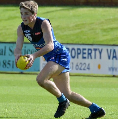 A football player in a blue and black guernsey kicks a ball on a field.
