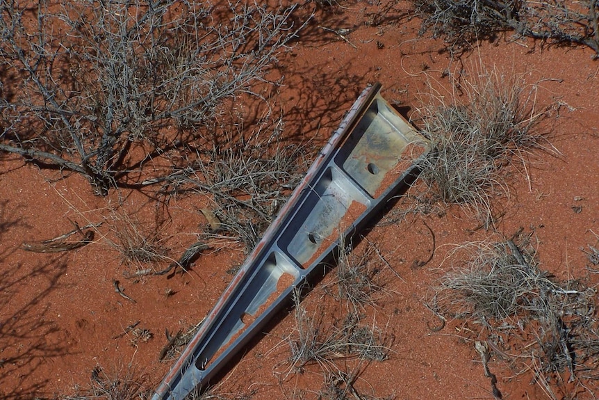 A triangular piece of metal rests on the ground surrounded by red dust