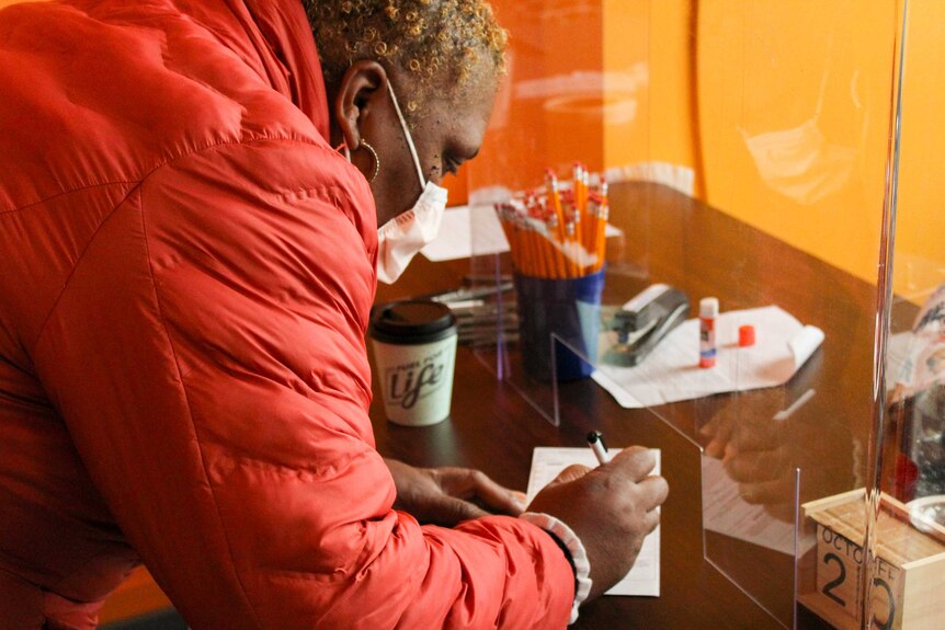 A woman signs a ballot on a desk