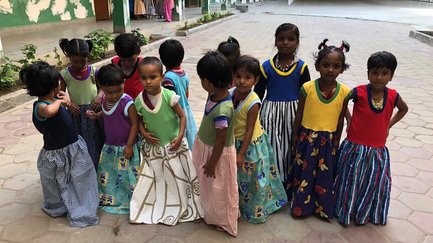 A group of Indian girls in brightly colour dresses gather in front of the camera.