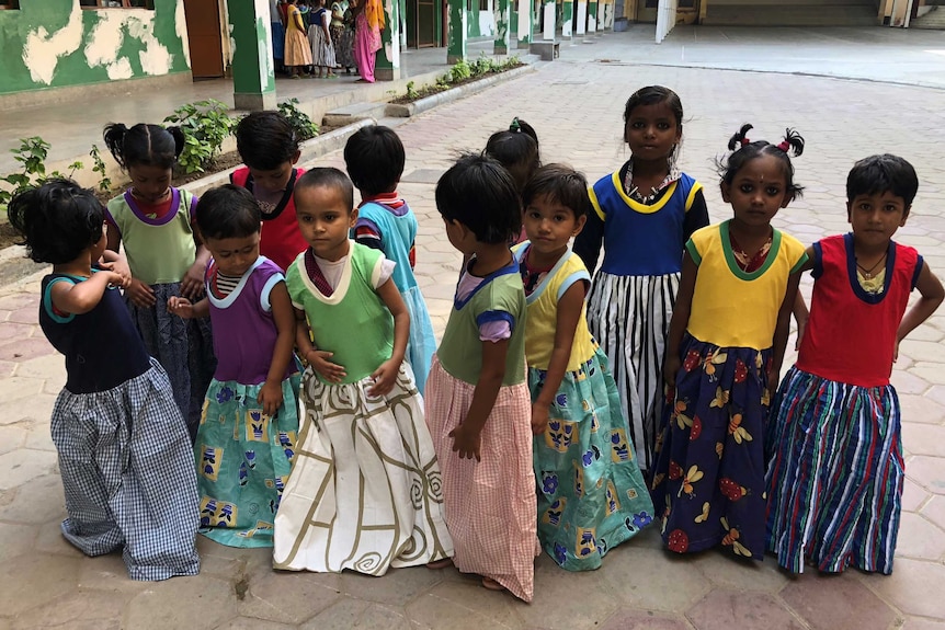 A group of Indian girls in brightly colour dresses gather in front of the camera.