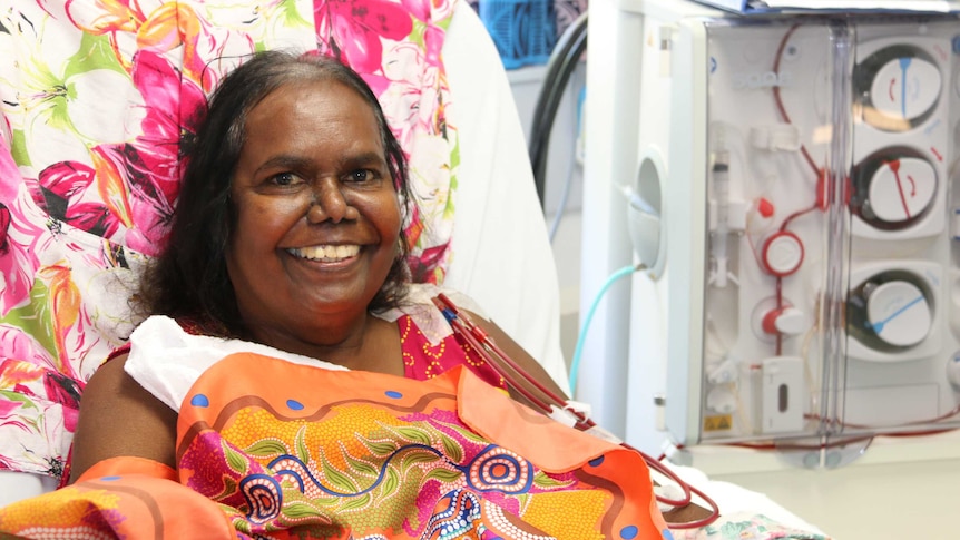 A woman lies in bed undergoing dialysis treatment.