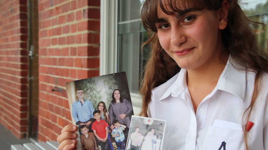 Student Rita Yousif poses for a photo in her school uniform holding family photographs from her life in Iraq.