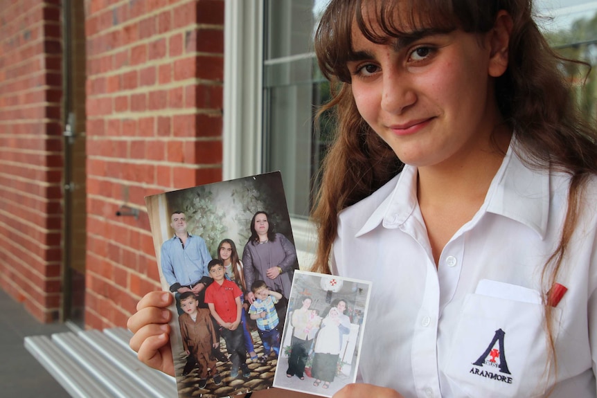 Student Rita Yousif poses for a photo in her school uniform holding family photographs from her life in Iraq.