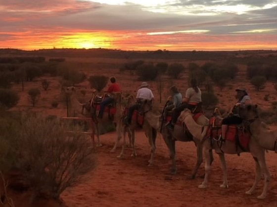 A red and yellow sunset in the desert with five people riding camels