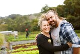 A smiling couple stand in a market garden.