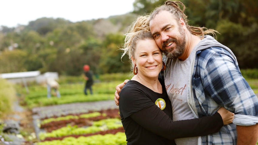 A smiling couple stand in a market garden.