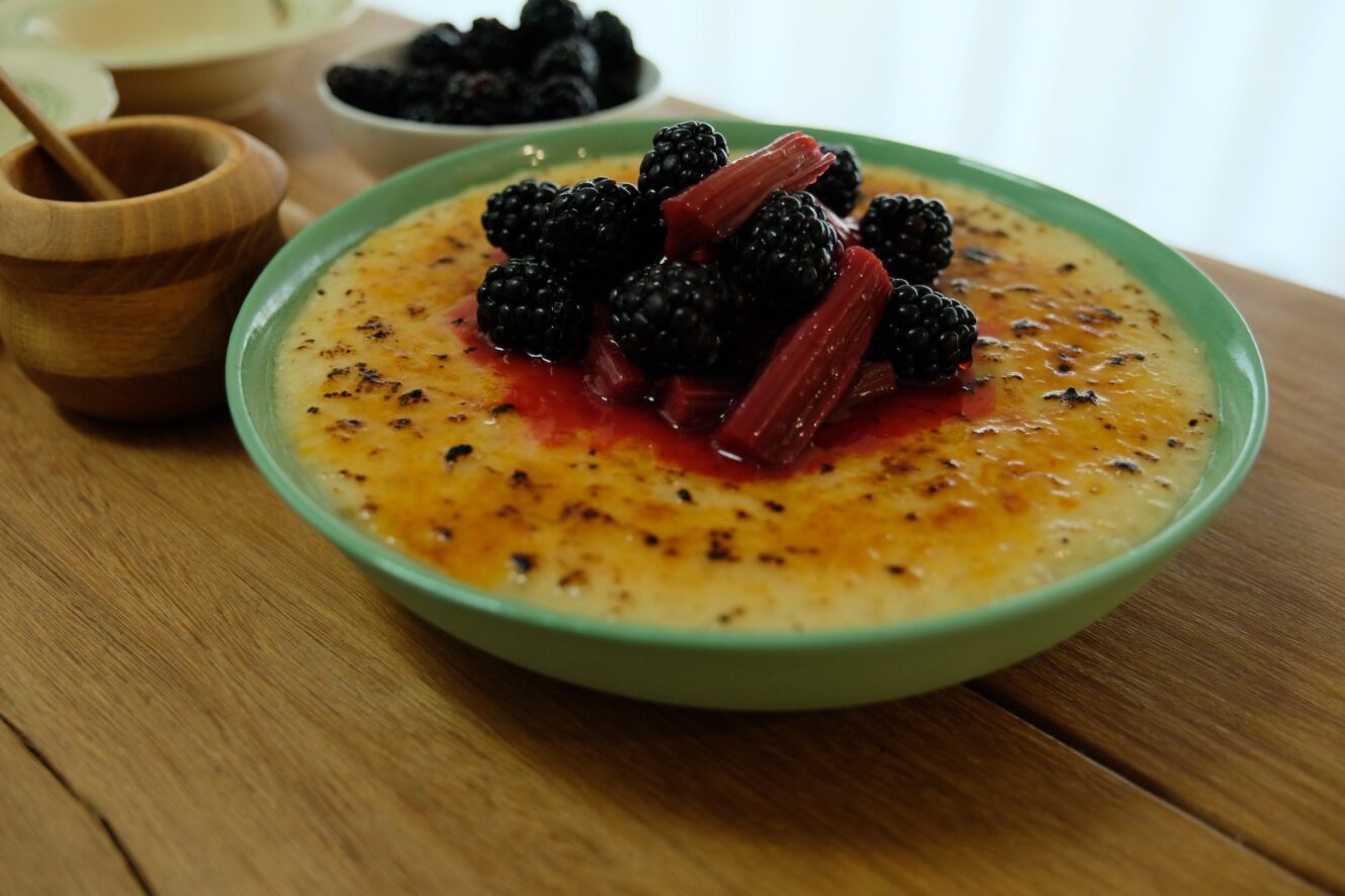 Rice pudding dessert with rhubarb and blackberries on a kitchen bench.