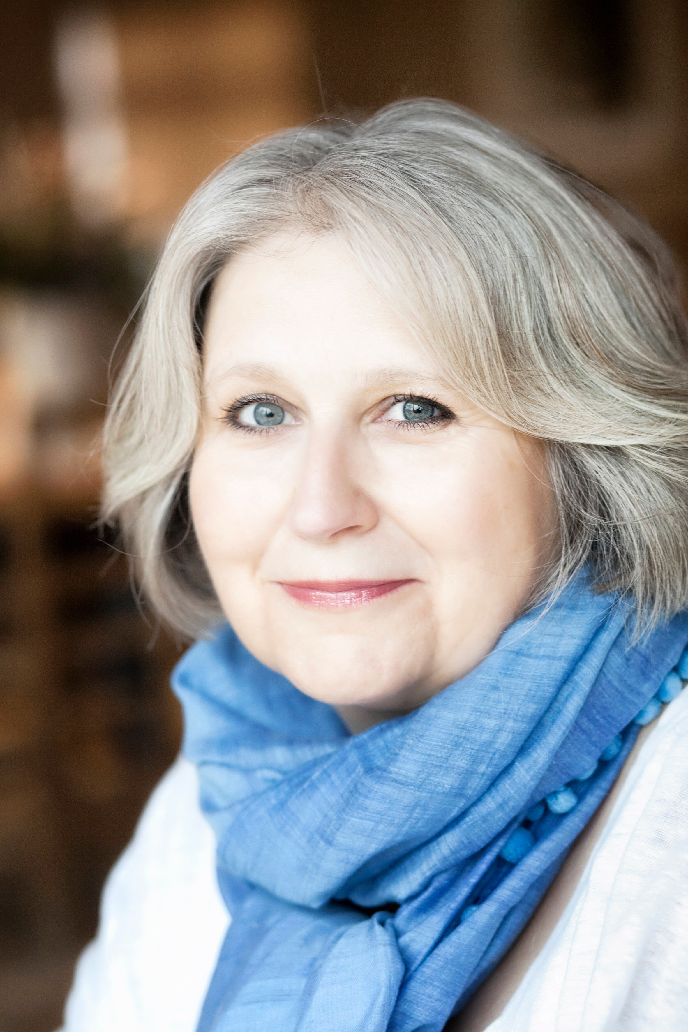 A headshot photo of a white middle-aged woman with short grey hair wearing a blue scarf and white shirt.