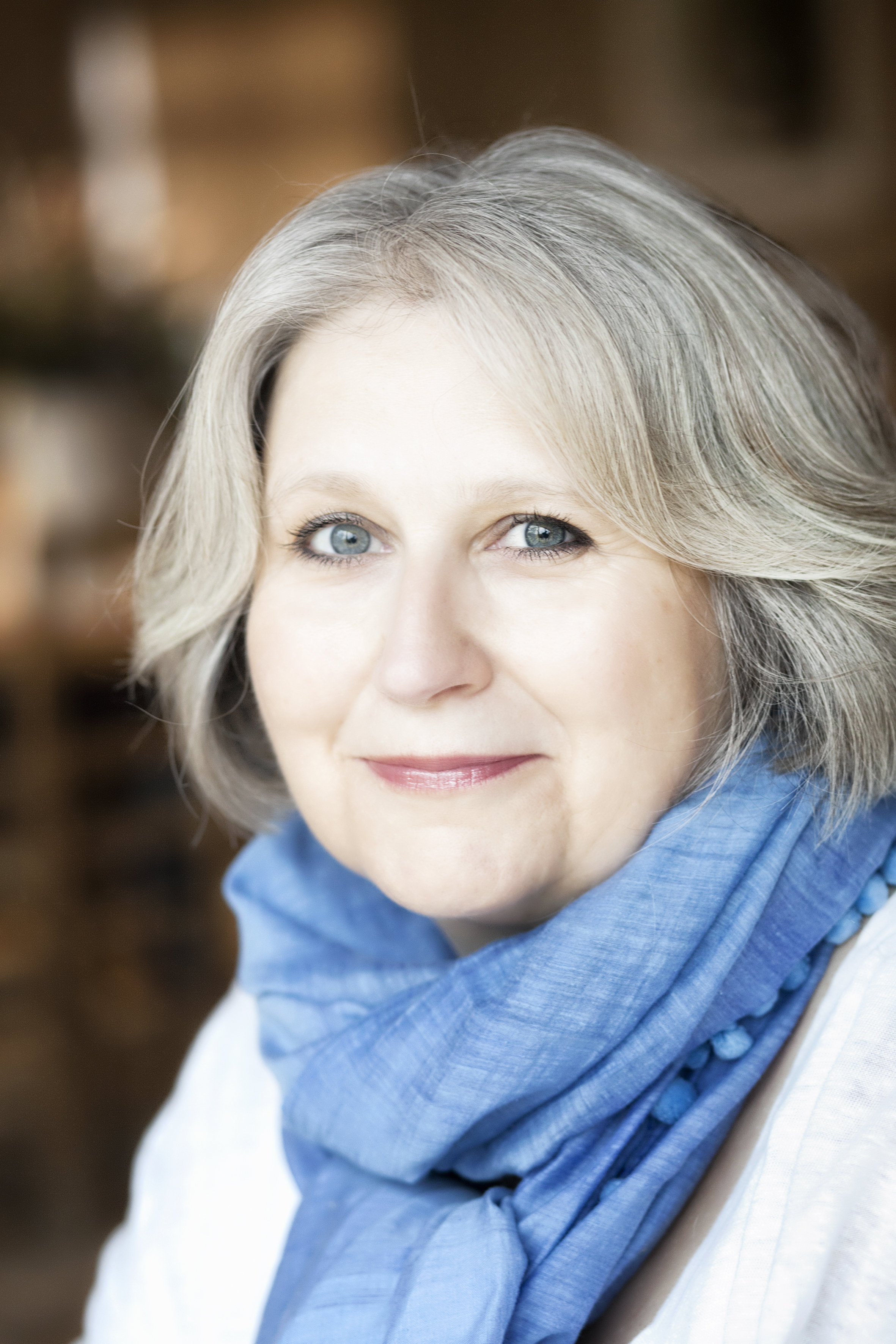 A headshot photo of a white middle-aged woman with short grey hair wearing a blue scarf and white shirt.