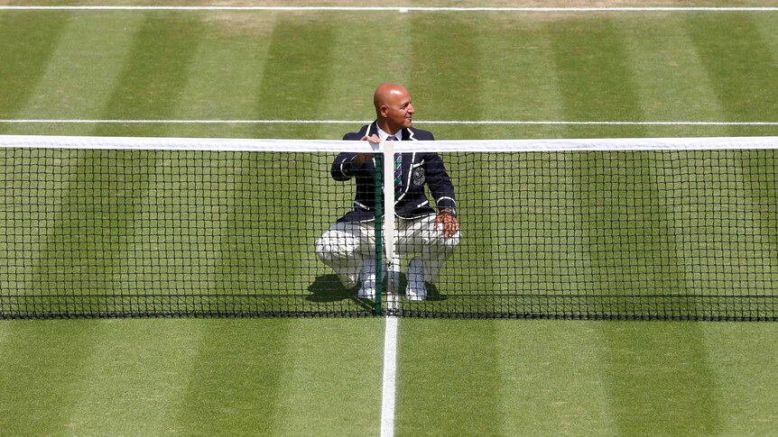 An official checks the net on an outside court at Wimbledon.