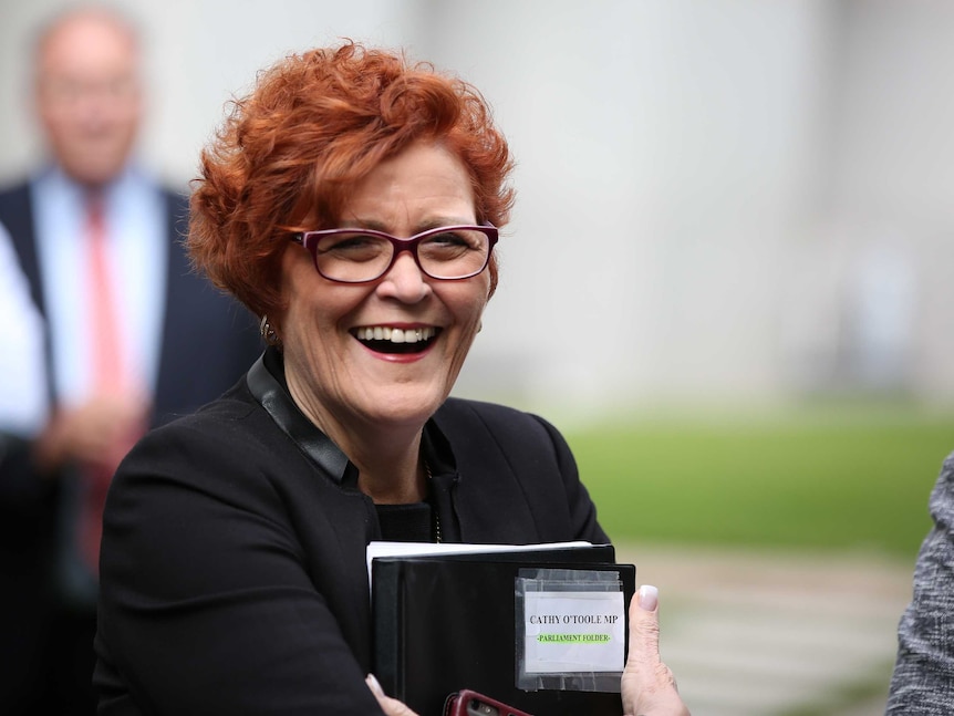 Cathy O'Toole laughs open-mouthed while clutching a book and stack of papers to her chest.