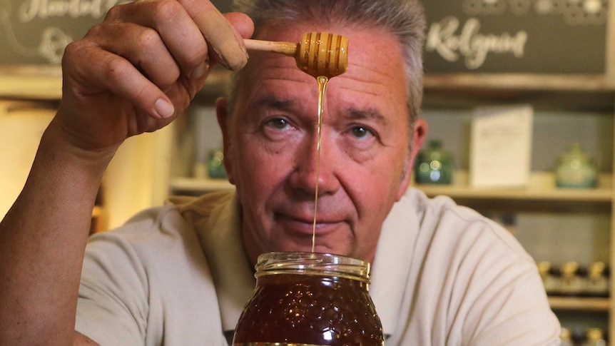 A man drips honey from a spoon into a jar.
