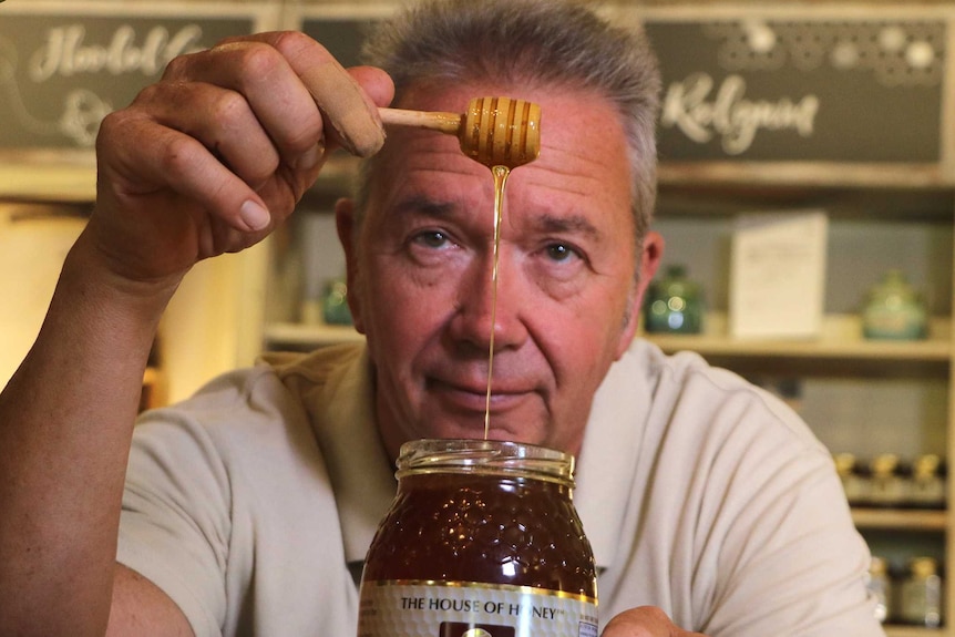 A man pours honey from a spoon into a jar.