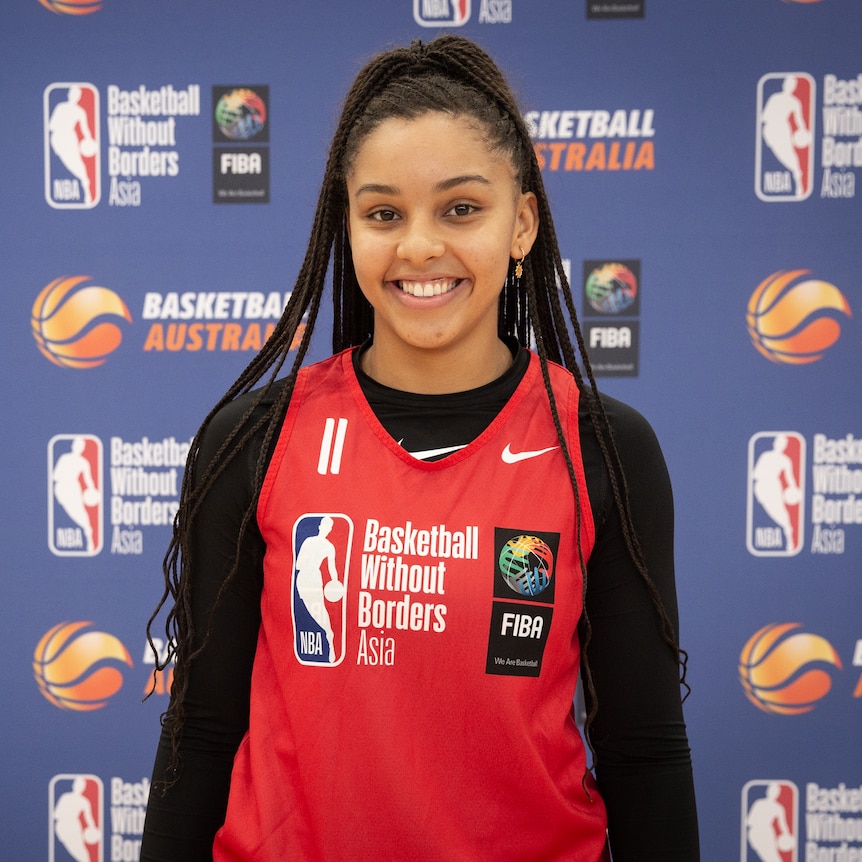 A woman wearing a basketball top smiles at the camera.