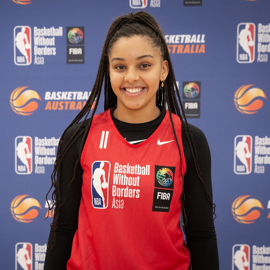 A woman weaing a basketball top smiles at the camera.