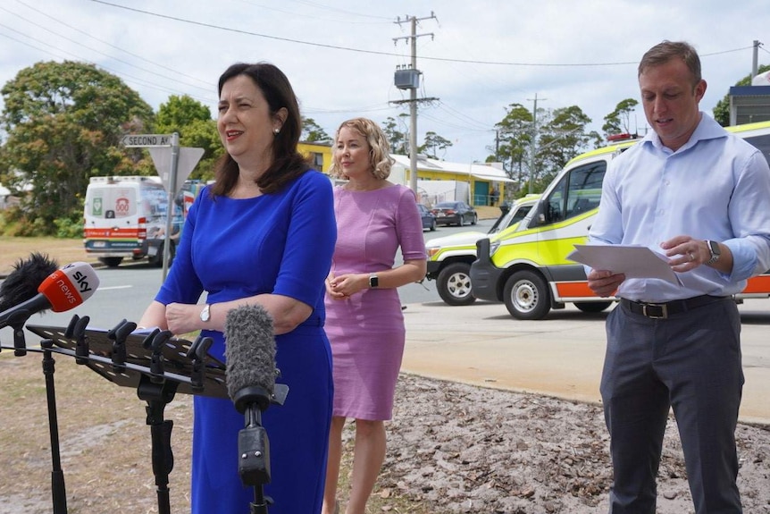 Palaszczuk stands in front of microphones with ambulances behind her.