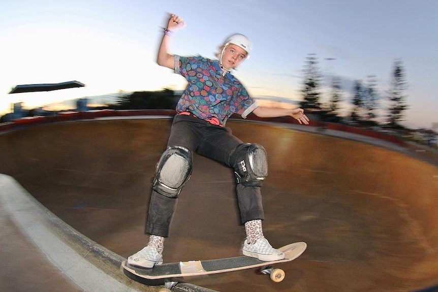 Action pic of a female skate board rider grinding along the coping of a skate bowl.