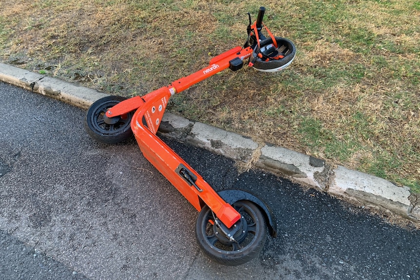 an orange e-scooter lying on the side of the road