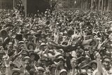 a crowd of faces fill the frame, some waving Australian flags. black and white