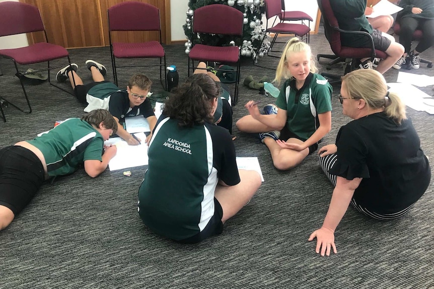 A group of people sit on the floor in a group.