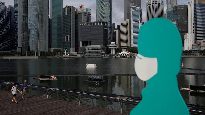 A aqua sign in the shape of a person wears a mask against a cityscape 