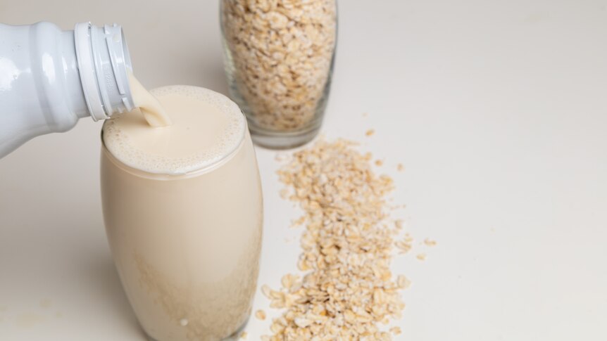 A glass of oat milk being poured next to a glass of rolled oats