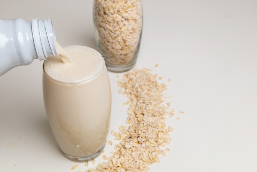 A glass of oat milk being poured next to a glass of rolled oats