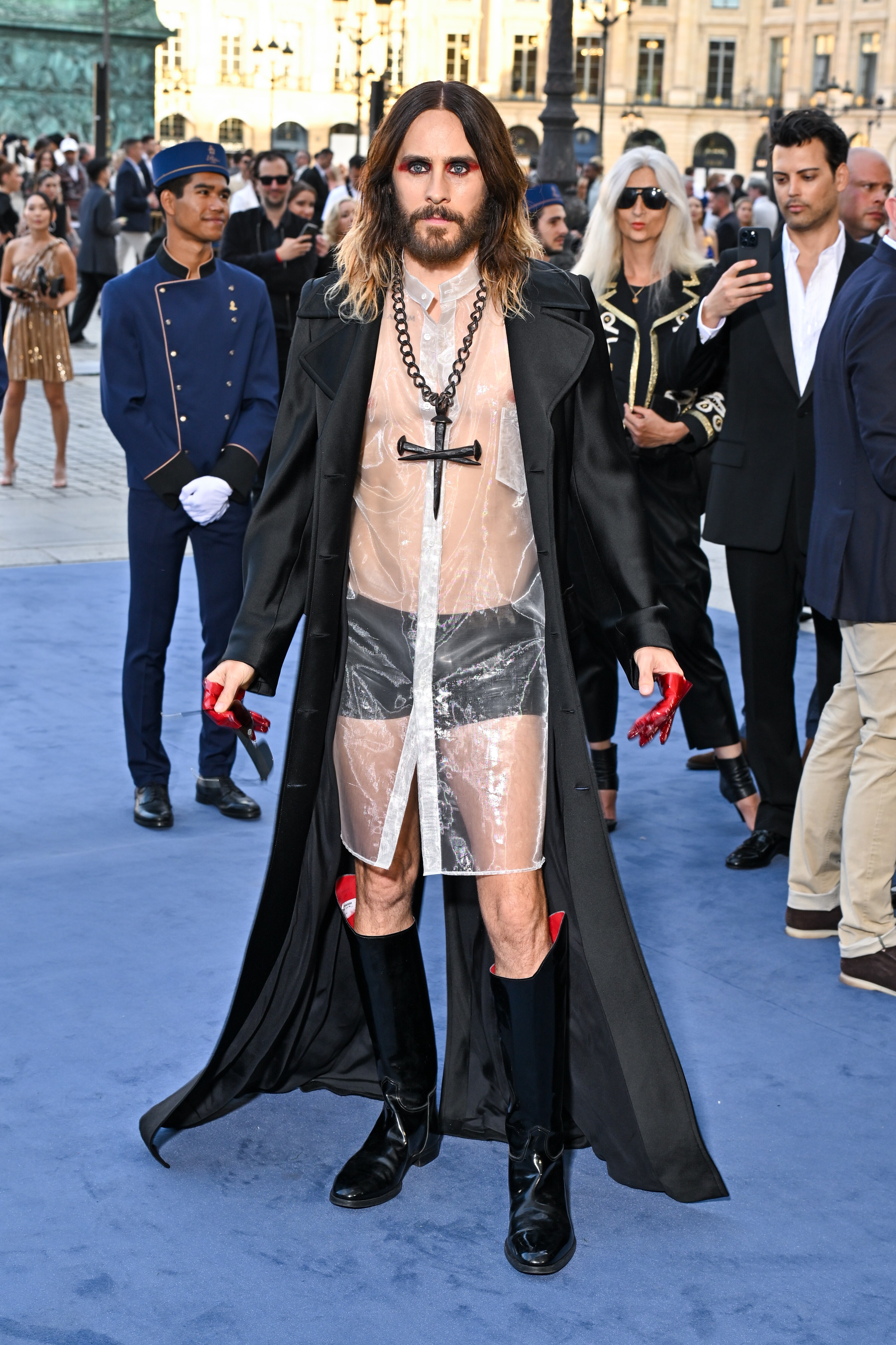 Jared Leto wears a see through plastic coat with black boots and boxer briefs and a black cross necklace