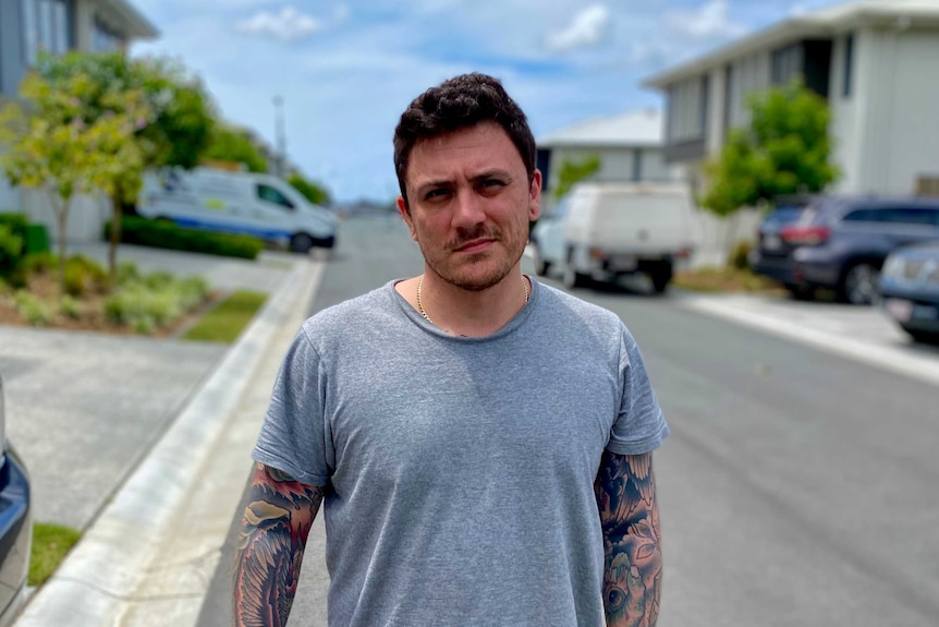 A man with tattoos down his arms stands in the street.