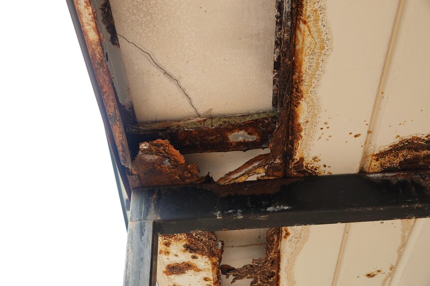 A damaged area on the underside of a metal roof, surrounded by rust.