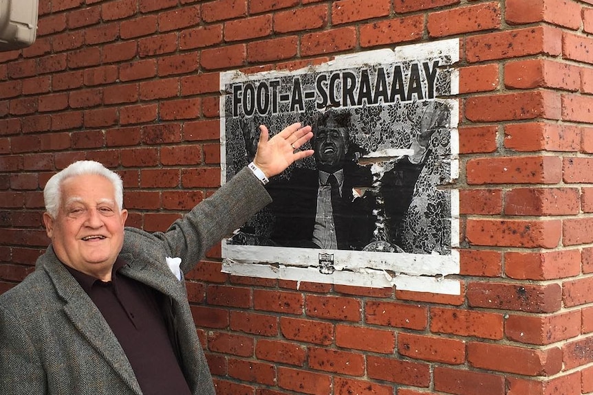 Franco Cozzo pointing to a poster with his face on it, beneath an unofficial lane signage reading Franco Cozzo lane.