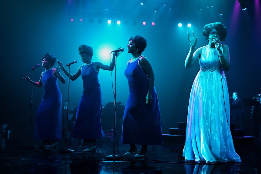 Jennifer Hudson and backing singer co-stars are coolly back-lit in silver and blue hues during an on stage performance.