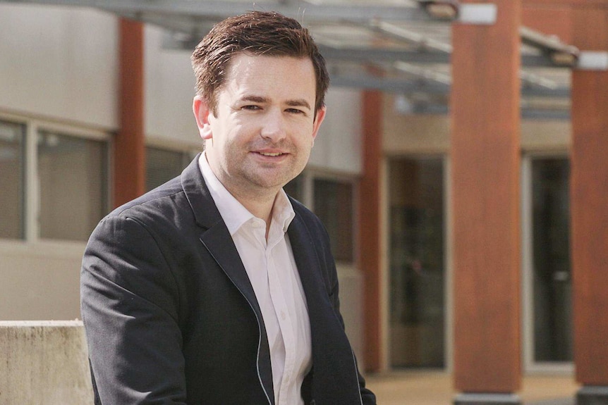 Dean Winter, wearing a suit jacket and white shirt, smiles at the camera