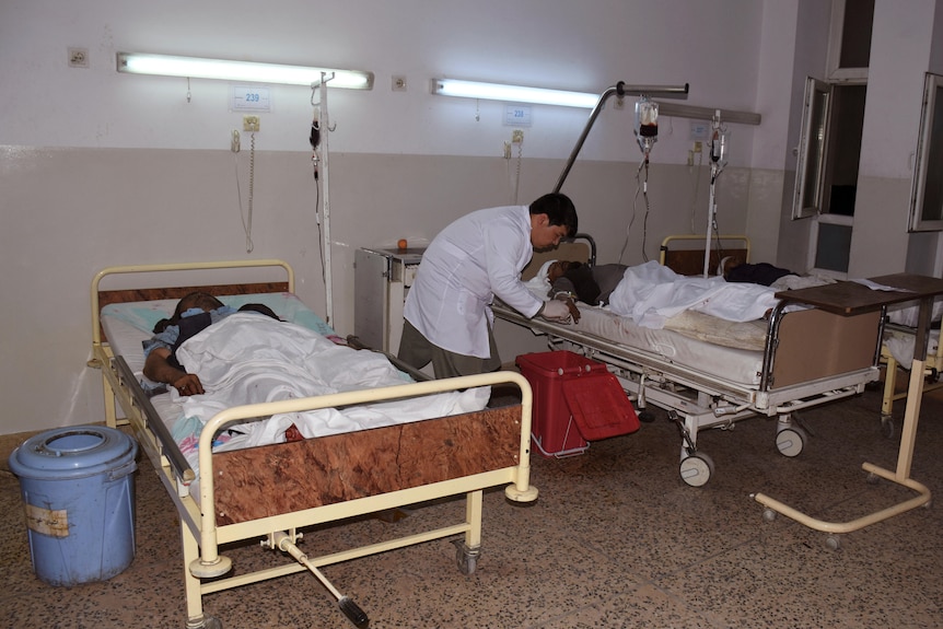 A man dressed in a white coat tends to one of two patients laying in modest beds