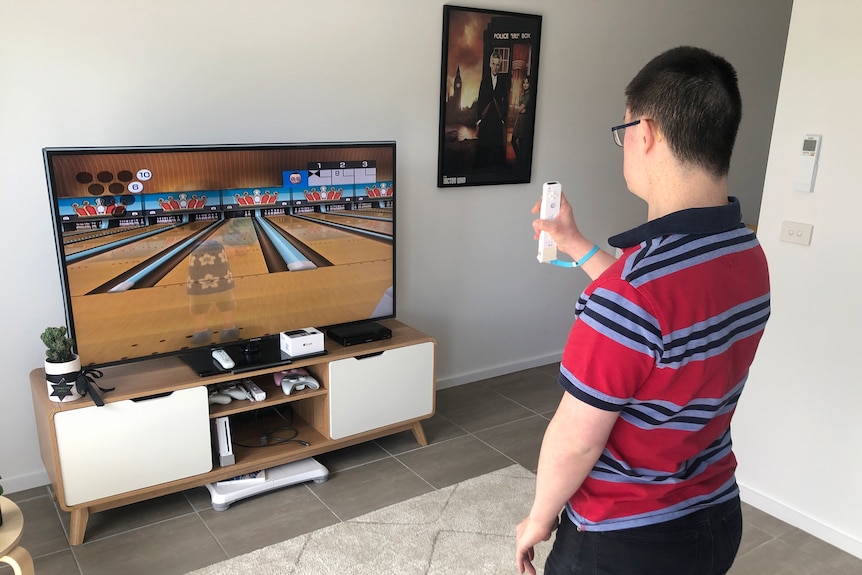 A dark haired man with glasses plays a video game on a Wii.