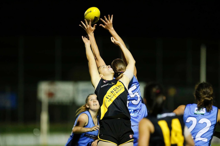 Two female footballers leap for a yellow football.