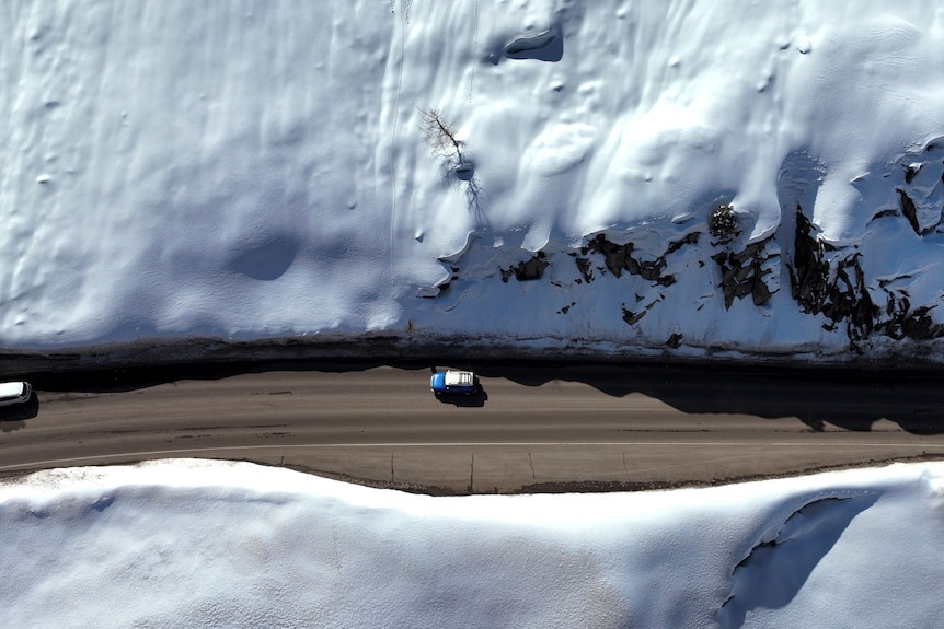 Cars drive on a road that is surrounded by snow on either side.