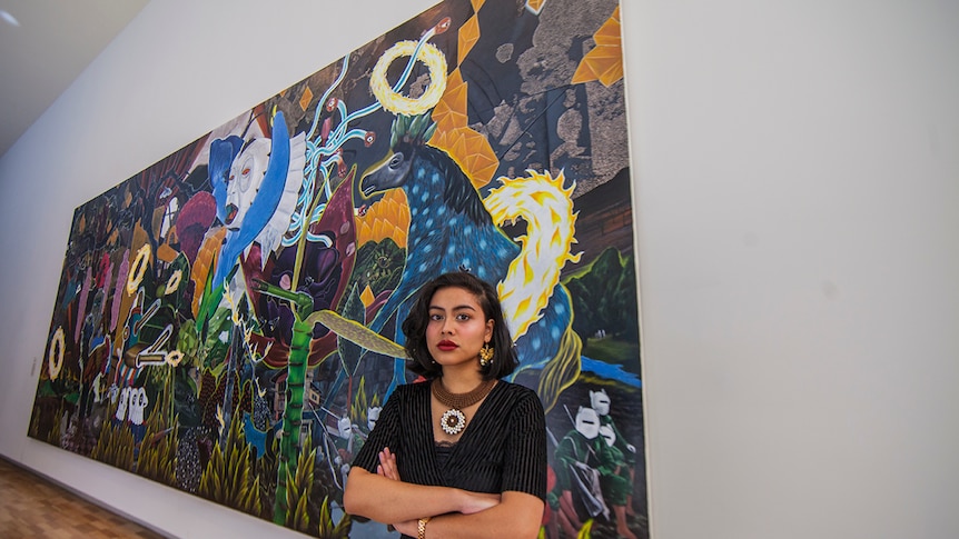 Poet Eunice Andrada stands in front of an acrylic on canvas artwork by Rodel Tapaya at the Art Gallery of New South Wales.