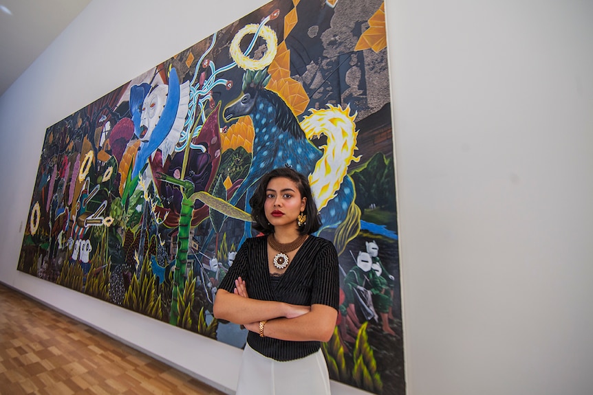 Poet Eunice Andrada stands in front of an acrylic on canvas artwork by Rodel Tapaya at the Art Gallery of New South Wales.