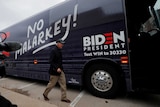 Joe Biden walks onto a navy blue bus with the slogan 'No Malarkey' pai8nted on the side.