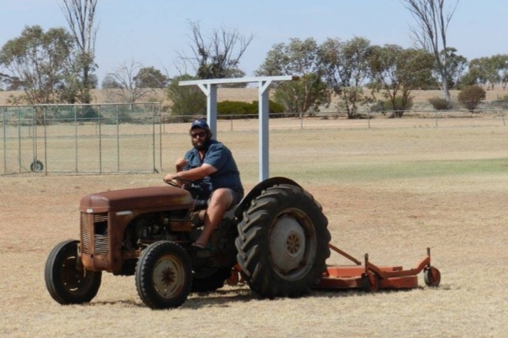 A man is driving a tractor over dry grass