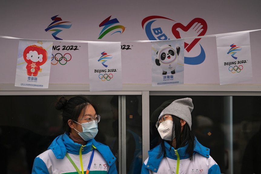 Two female volunteers wearing face masks chat with each other at an information booth.