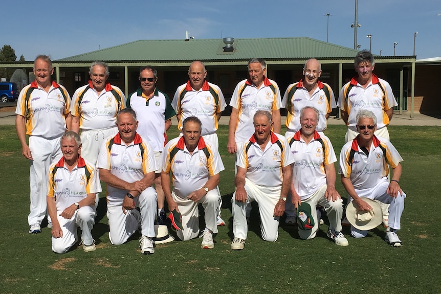 Thirteen men in cricket whites posing for their cricket team photo.