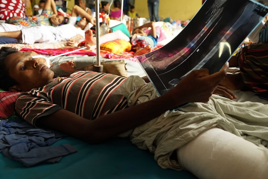 A young man lies on a hospital floor with many other refugees and looks at an x-ray of his leg.