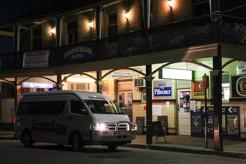 A white van with its headlights turned on outside a country pub at night