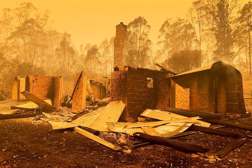 Rubble of a home burnt to the ground in bushfires with an orange and yellow glow in the air around