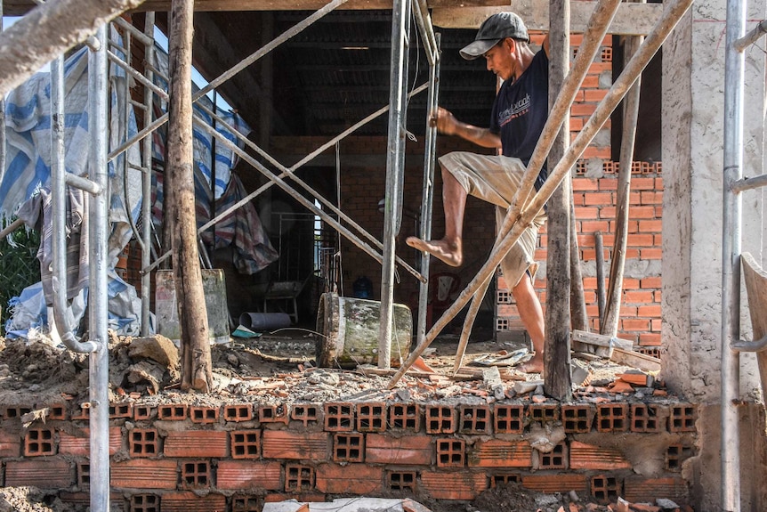 Tradie swings between scaffolding in bare feet above rubble